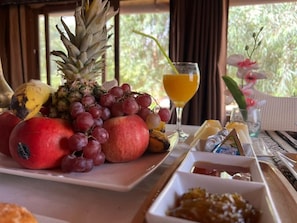 Uma mesa de café da manhã com frutas, um copo de suco de laranja e um arranjo de flores.