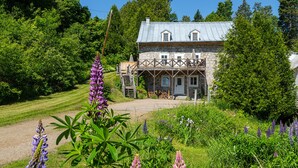 Een stenen huis met een balkon, omringd door weelderige begroeiing en bloeiende planten.