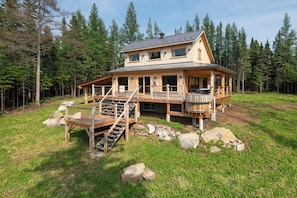 A wooden cabin with a deck, stairs, and a hot tub.