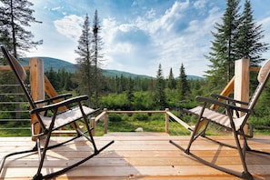 A wooden deck with two rocking chairs facing a forested mountain landscape.