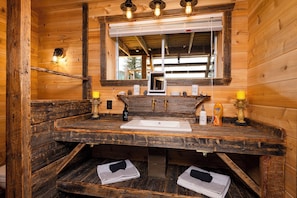 A rustic wooden bathroom with a sink, mirror, and two towels.