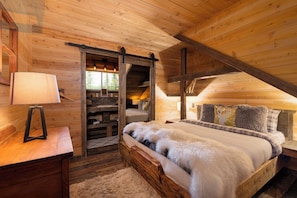 A cozy log cabin bedroom with a bed, a nightstand, a lamp, and a wooden ceiling.
