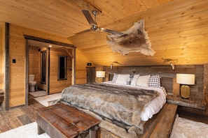 A log cabin bedroom with a bed, a bench, a ceiling fan, and a fur rug.