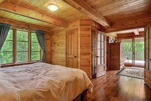Habitació d'una cabana de fusta amb un llit, un armari i una porta que dona a un balcó.