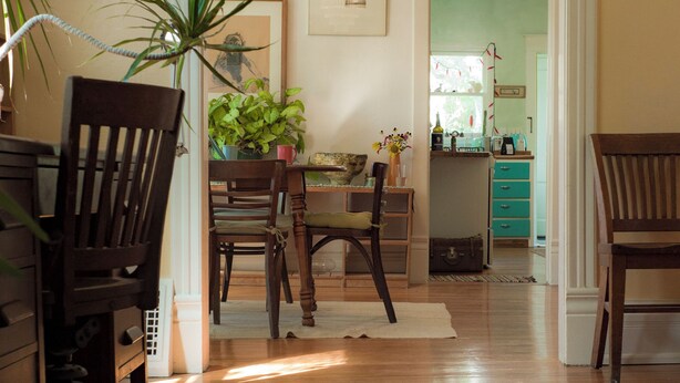 Un comedor con sillas de madera, una mesa y una araña. Se ve una cocina al fondo.