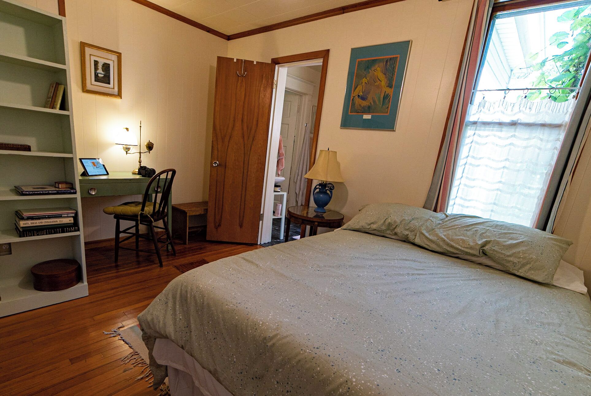 Une chambre à coucher avec un lit, un bureau avec une chaise, une bibliothèque et une fenêtre avec des rideaux.