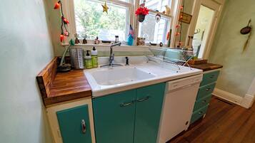 Une cuisine dotée d’un évier à deux bacs, d’un plan de travail en bois, de meubles de couleur turquoise et d’une fenêtre décorée.
