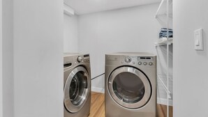 Une buanderie équipée de deux machines à laver à chargement frontal en acier inoxydable et d’une étagère blanche où sont pliés les vêtements.