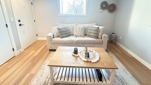 Un salon avec un canapé beige, une table basse en bois et une fenêtre équipée de stores.