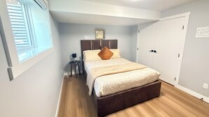 Une chambre à coucher avec un lit, une table de chevet, une fenêtre, un luminaire au plafond et une porte.