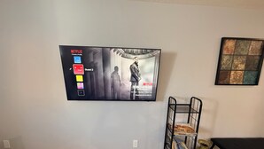 Un téléviseur fixé au mur affiche un profil Netflix avec une affiche du film « Let the Roast » de Kevin Hart.