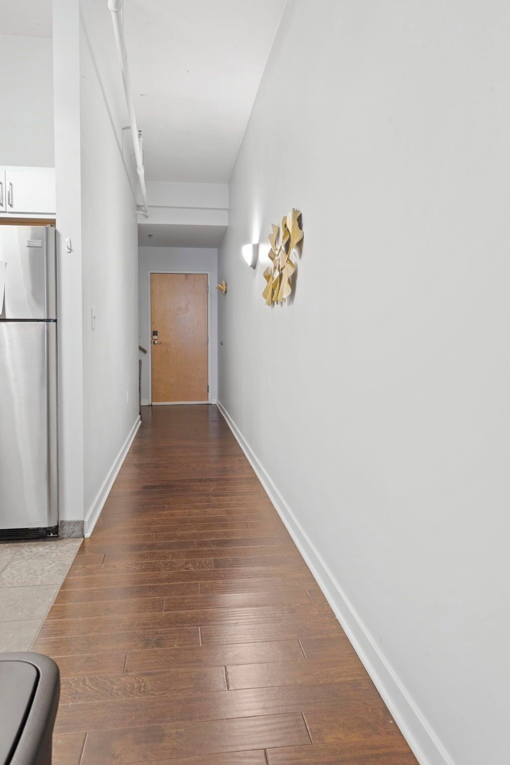 A hallway with a wooden floor, white walls, and a door at the end.