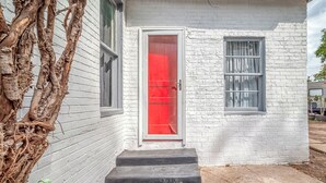 A white brick building with a red door and a small porch.