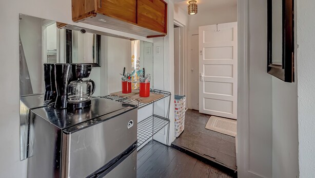 A compact kitchen with a stainless steel refrigerator, a coffee maker, and red mugs on the counter.