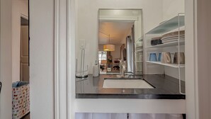 A kitchen with a black countertop, white cabinets, and a hanging light fixture.