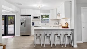 A modern kitchen with white cabinets, a stainless steel refrigerator, a microwave, and a large island with bar stools.
