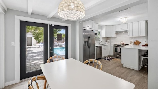A modern kitchen with white cabinets, a stainless steel refrigerator, and a dining area with a white table and wicker chairs.
