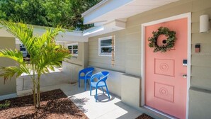 A house with a pink door, a small porch with blue chairs, and a potted plant.