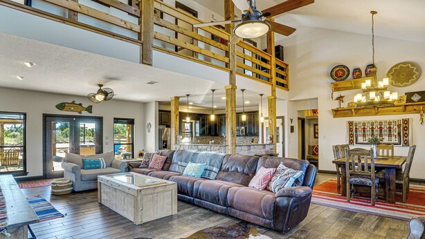 A spacious living room with a large leather sofa, wooden ceiling beams, and a dining area with a wooden table and chairs. - Hot Tub + Fire Pit: Possum Kingdom Lake Retreat! (Strawn)