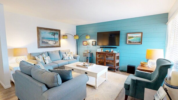 A living room with a blue wall, a sofa, a coffee table, a TV, and a chair. - Beach Access Across the Street, Shared Heated Pool (Corpus Christi)