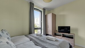 A bedroom with a bed, a TV, a wardrobe, and a window with curtains. - Okrzei Residence - Nadmorska Bryza by GA (Sopot)