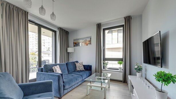 A modern living room with a blue sofa, a glass coffee table, and a white TV stand. - Okrzei Residence - Nadmorska Bryza by GA (Sopot)