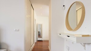 A hallway with a wooden floor, white walls, a white vanity with a mirror, and a door with blinds.