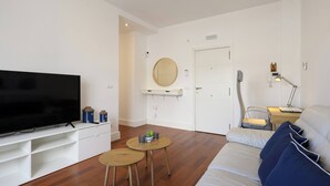 A modern living room with a flat-screen TV, a sofa, two small round tables, and a wooden door.