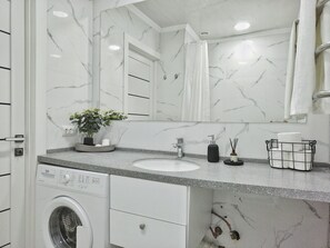 Une salle de bain moderne avec un pare-feu en marbre, un lave-linge encastré, un évier et un grand miroir.
