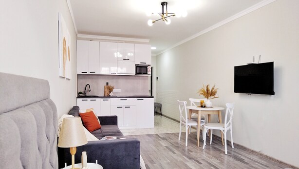 A modern living room with a grey sofa, a small table with a lamp, and a TV mounted on the wall. - Cozy "Spica" apartment with mountain view in Almaty + AC, WiFi (Almaty)