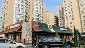 A McDonald's restaurant with a green awning and a signboard, located in front of a tall residential building. - Cozy "Spica" apartment with mountain view in Almaty + AC, WiFi (Almaty)