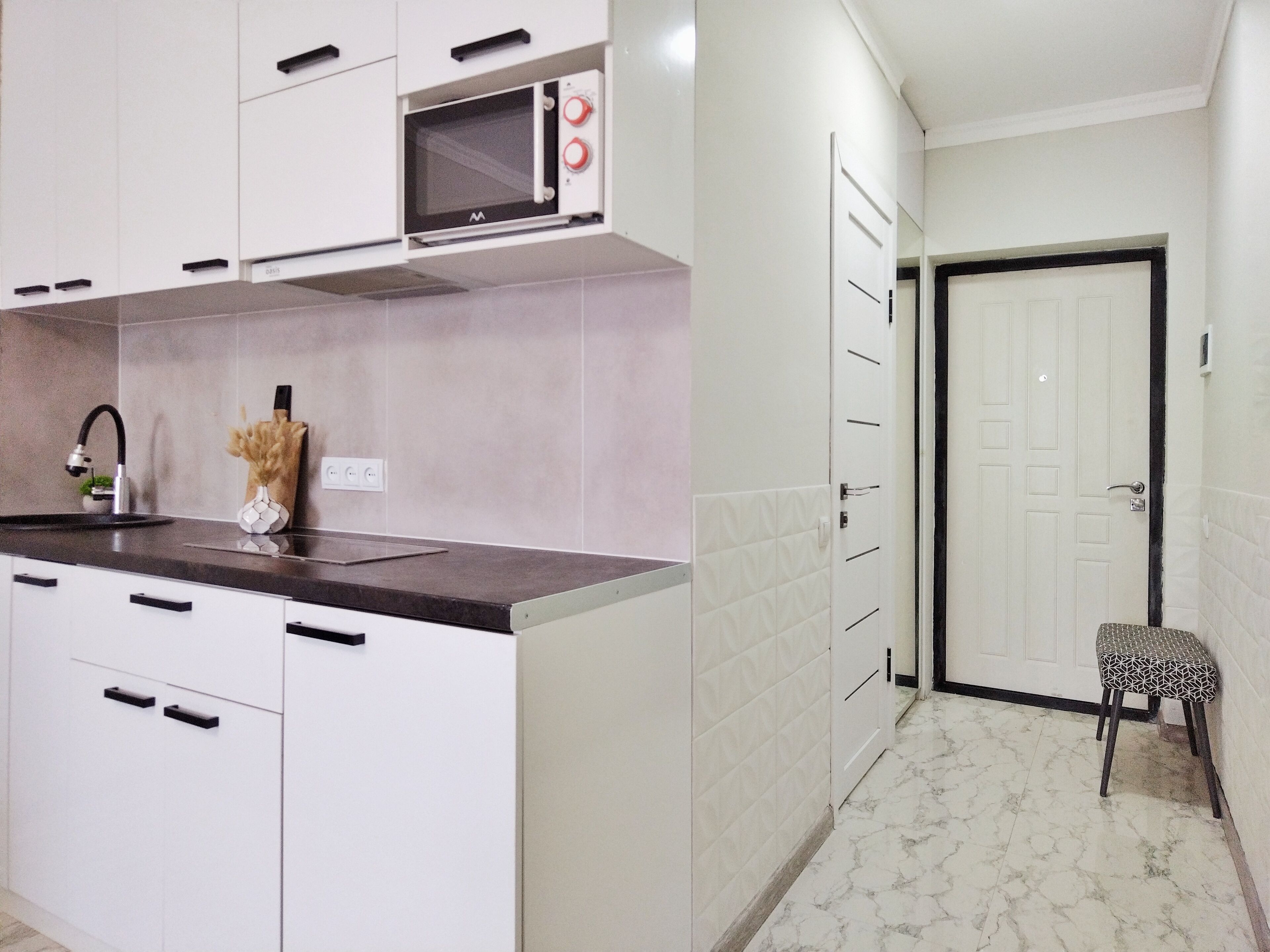 A modern kitchen with white cabinets, a black countertop, a microwave, and a sink.