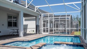 A swimming pool with a hot tub, surrounded by a covered patio area with chairs and a table. - Spacious Themed 8BR Villa at Champions Gate – Resort full Access, Near Disney! (Four Corners)