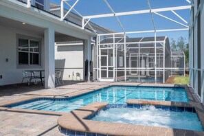 Une piscine avec un jacuzzi, entourée d’un patio couvert comprenant des chaises et une table.