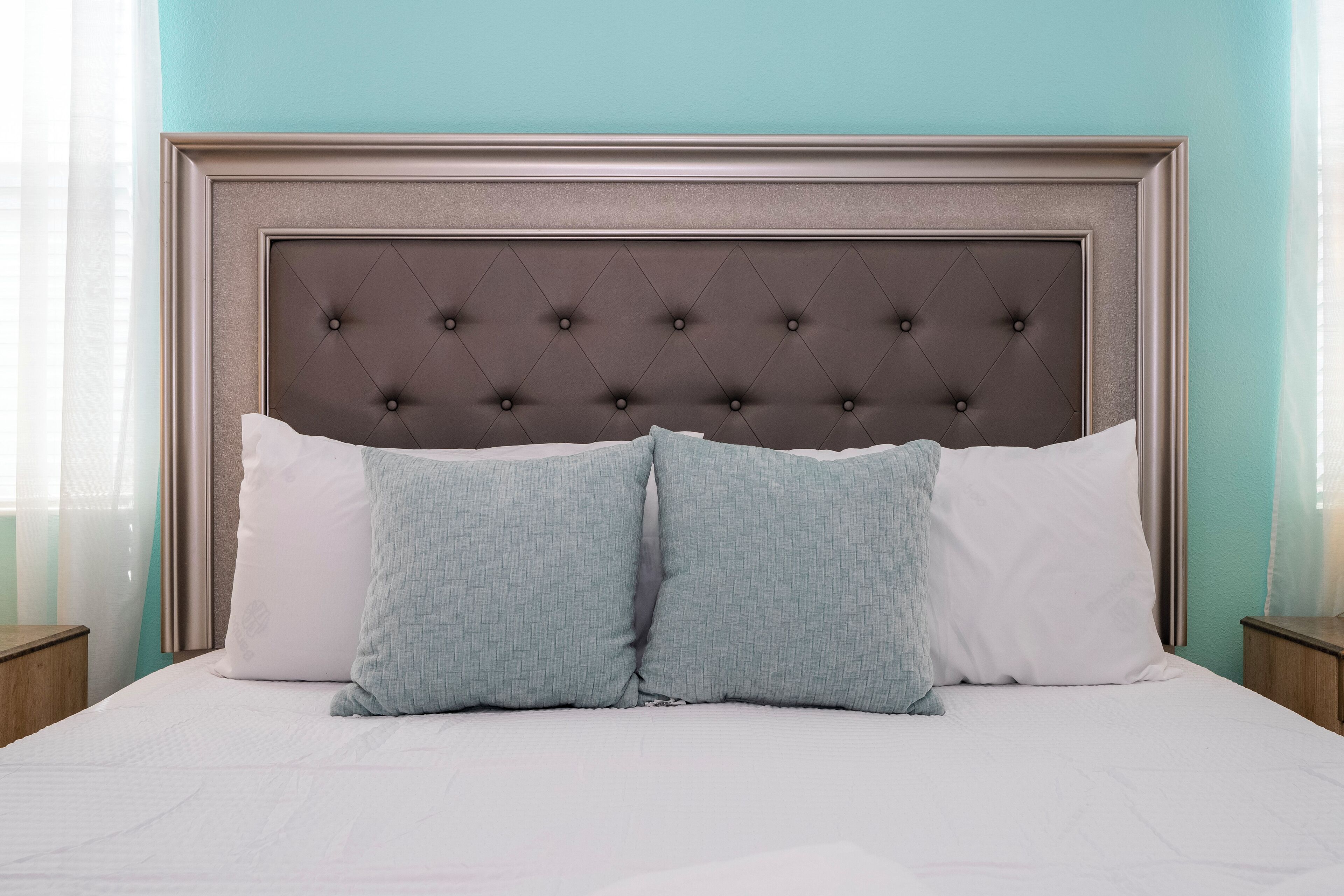 Una cama bien hecha con un cabecero capitonado, dos almohadas y una mesita de noche de madera a su lado.