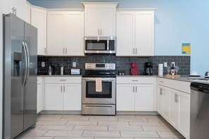 A modern kitchen with white cabinets, stainless steel appliances, and a tiled backsplash. - Spacious Themed 8BR Villa at Champions Gate – Resort full Access, Near Disney! (Four Corners)