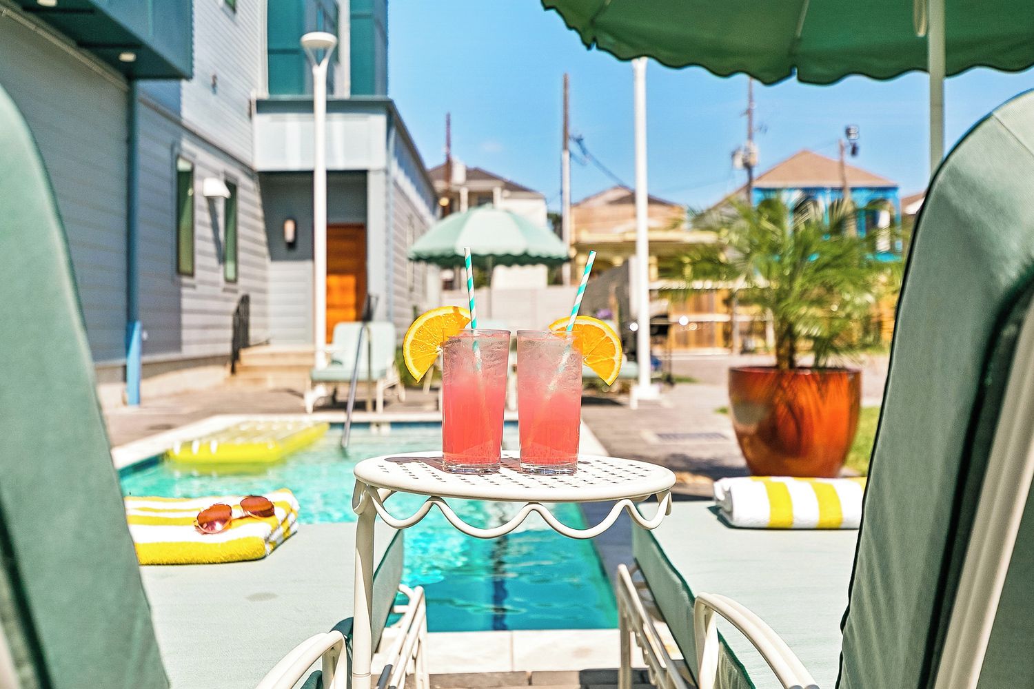 Vista de la piscina con una mesa que sostiene dos bebidas, piscina y un edificio al fondo.