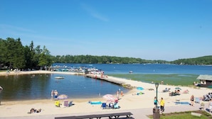 A lakeside beach with boats, a dock, and people relaxing.