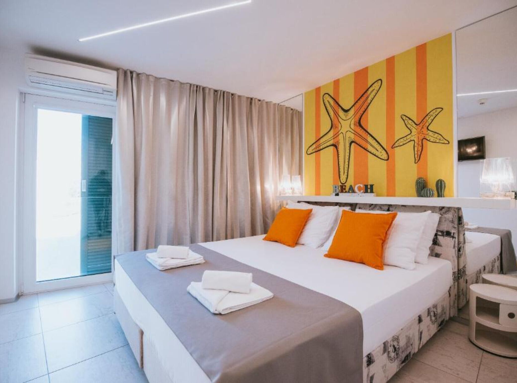 A modern hotel room with a large bed, a view of the beach, and a starfish mural on the wall.