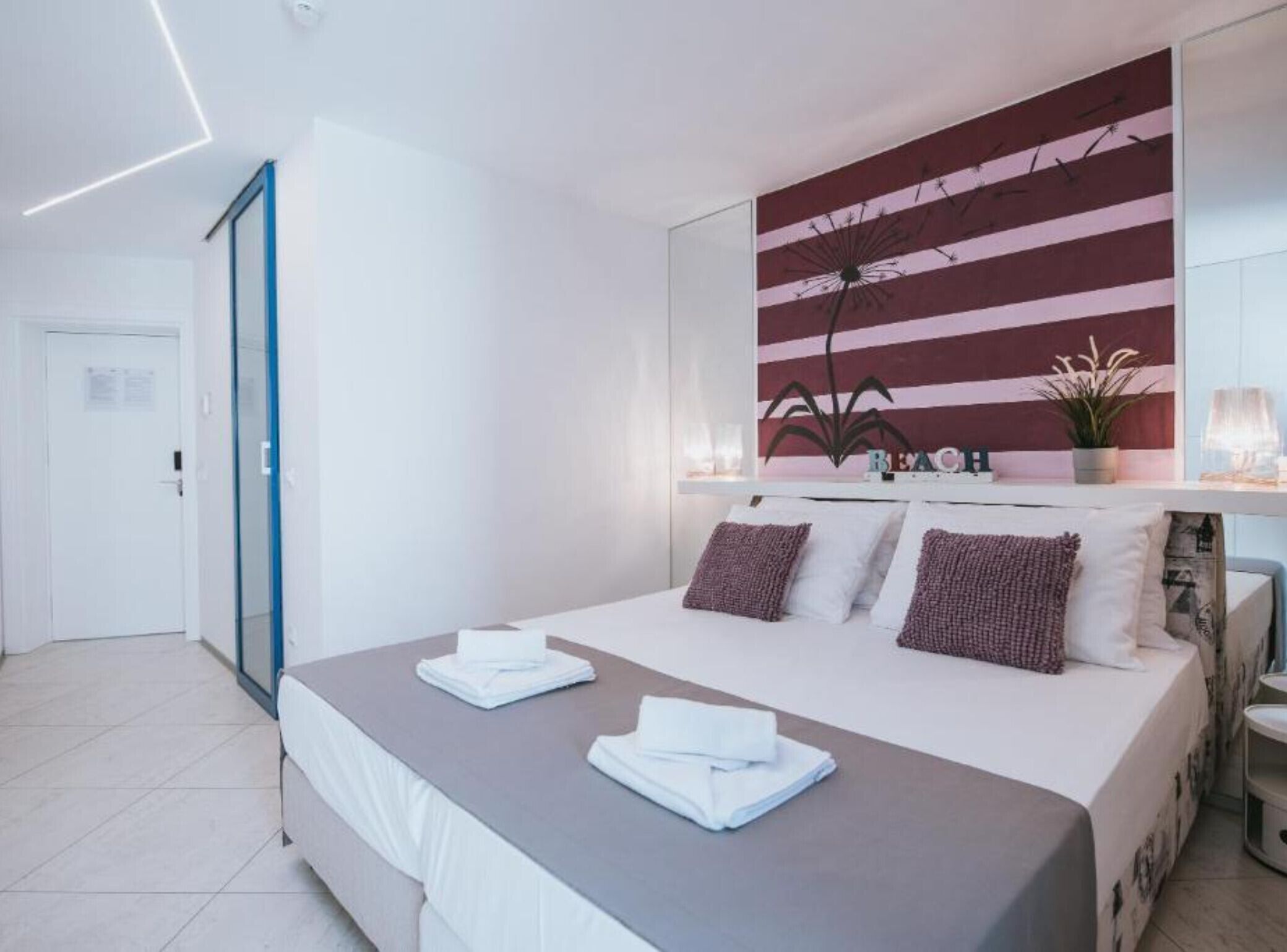 A modern hotel room with a large bed, a bedside table with a lamp, and a wall-mounted artwork.