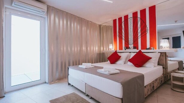 A modern hotel room with a large bed, a bedside table, a mirror, and a view of the outdoors. - Bed in Eight Bed Mixed Dormitory Room 1 (Novalja)