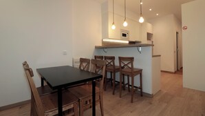 Un comedor con una mesa negra y sillas de madera, una cocina con microondas y lámparas colgantes.