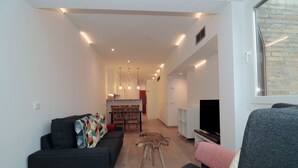 Una sala de estar moderna con un sofá, una silla, un televisor y un comedor con una mesa y sillas.