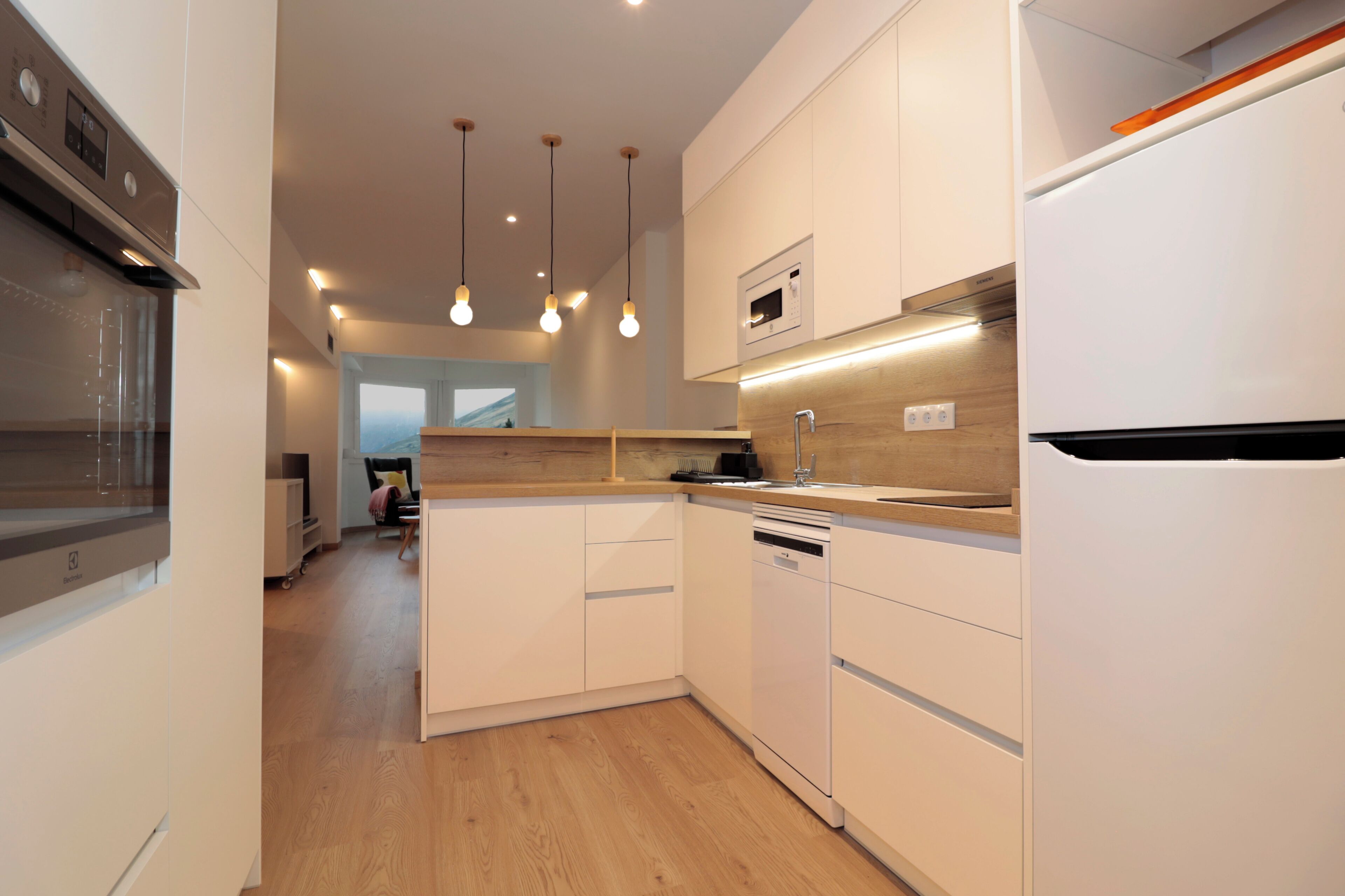 Een moderne keuken met witte kastjes, een ingebouwde oven, een magnetron en hangende lampen.