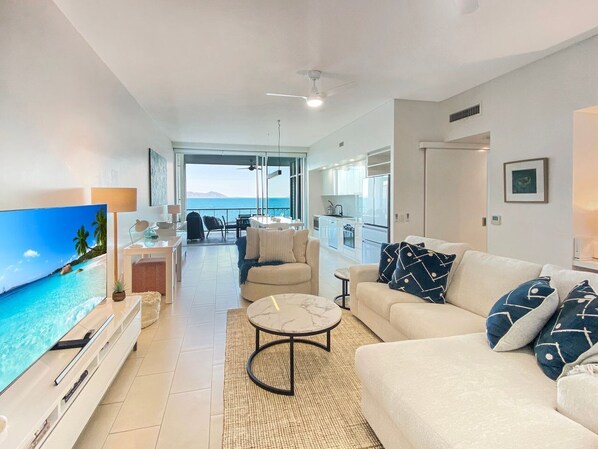 Een moderne woonkamer met een grote televisie, een bank, een salontafel en een eethoek met uitzicht op de oceaan.