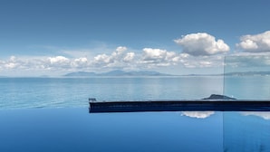Vista despejada del mar y montañas lejanas, protegida por una barandilla de cristal.