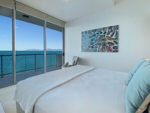 Een slaapkamer met een groot bed, een stoel, een telefoon en een schilderij. Het heeft een balkon met uitzicht op de zee.