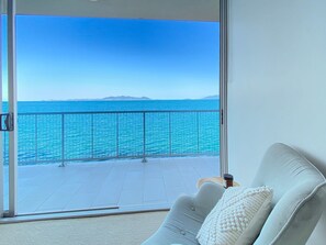 A balcony with a view of the sea, a white sofa with a cushion, and a small table with a candle. - 1 Bright Point Apartment 5101 (Nelly Bay)