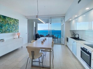 A modern kitchen with a dining area, large windows, and a view of the sea. - 1 Bright Point Apartment 5101 (Nelly Bay)