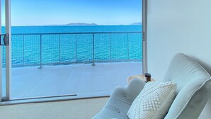 Un balcón con vista al mar, un sofá blanco con un cojín y una pequeña mesa con una vela.